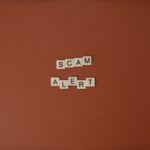 Kostki Scrabble tworzące napis Scam Alert na brązowym tle