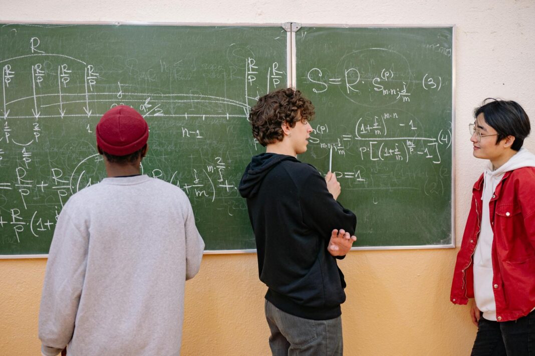 Trójka uczniów przy tablicy omawia zadania z matematyki
