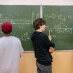 Trójka uczniów przy tablicy omawia zadania z matematyki
