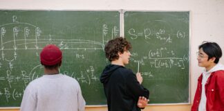 Trójka uczniów przy tablicy omawia zadania z matematyki