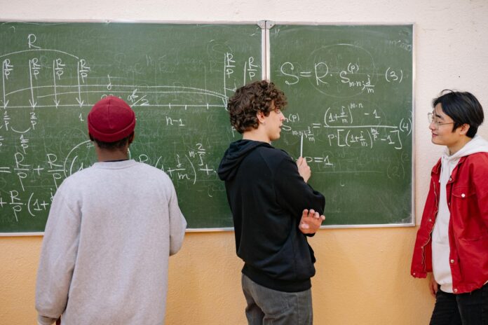 Trójka uczniów przy tablicy omawia zadania z matematyki