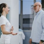 Uśmiechnięta pielęgniarka rozmawia z seniorem podczas wizyty lekarskiej