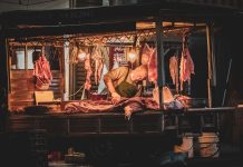 Oszustwa pig butchering – jak azjatyckie syndykaty prowadzą fabryki scamów? Rzeźnik krojący mięso na nocnym targu przy ciepłym świetle