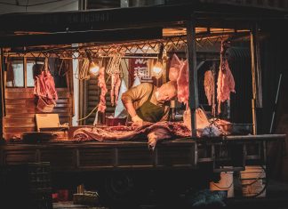 Oszustwa pig butchering – jak azjatyckie syndykaty prowadzą fabryki scamów? Rzeźnik krojący mięso na nocnym targu przy ciepłym świetle